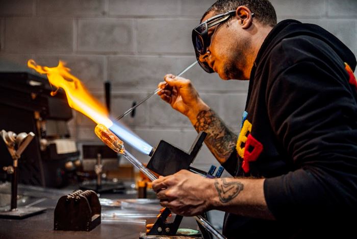 Man working in shop blowing glass with torch